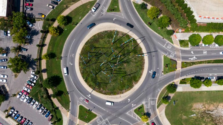 Drone shot of a city roundabout with vehicles, showcasing traffic flow and urban design.